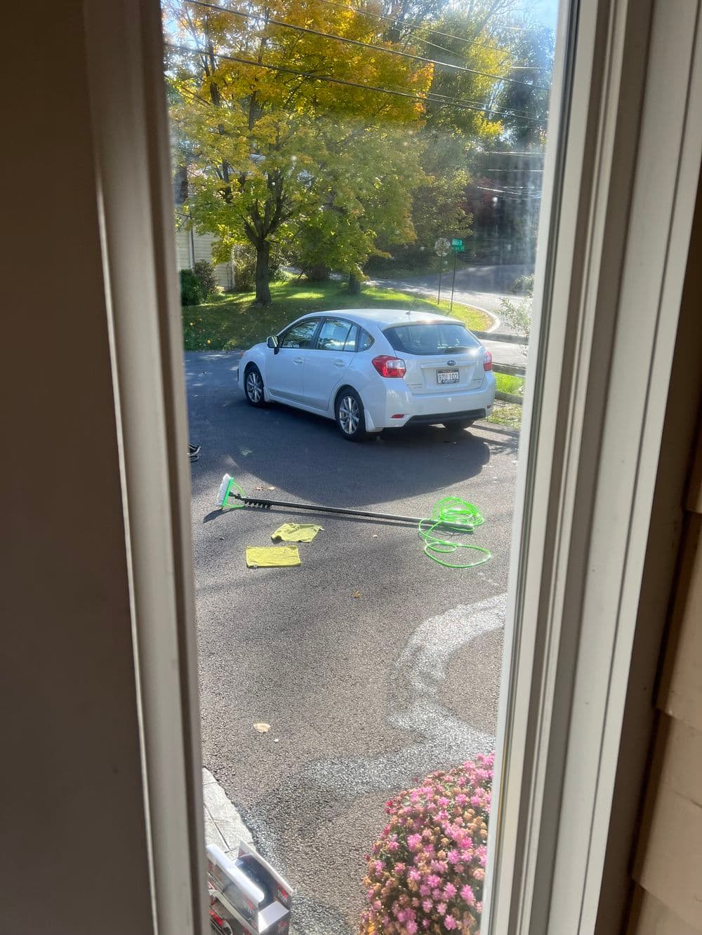 View of a white car parked outside, with garden tools and autumn foliage in the background.